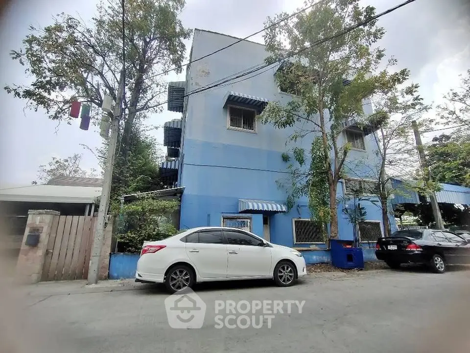Charming blue building with street view and parked cars, surrounded by lush greenery.