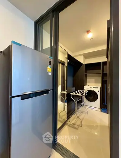 Modern kitchen with stainless steel fridge and washing machine in sleek apartment.