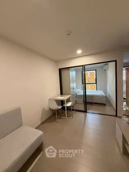 Modern apartment interior with cozy living area and bedroom separated by glass doors.