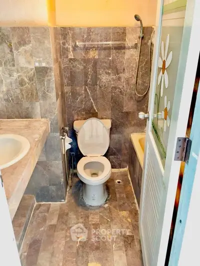 Compact bathroom with marble tiles and floral shower door
