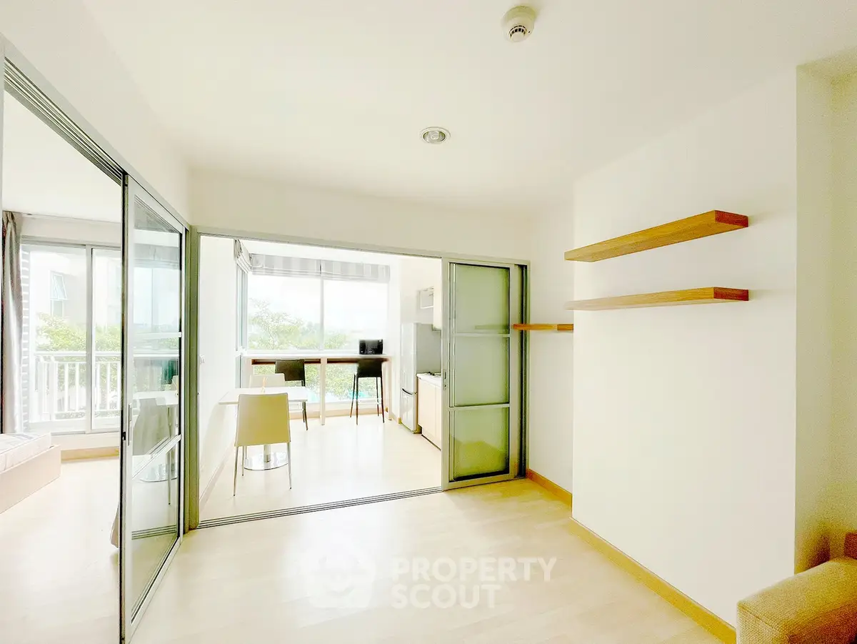 Bright modern apartment with open layout and sliding glass doors, featuring a cozy dining area and minimalist shelves.