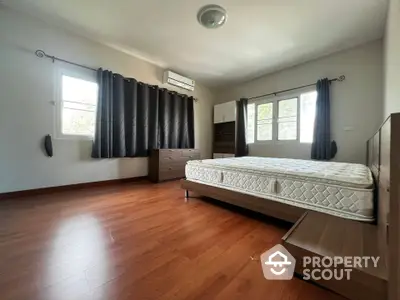 Spacious bedroom with wooden flooring and large windows for natural light.