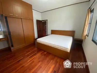 Spacious bedroom with wooden flooring and built-in wardrobe in modern apartment.