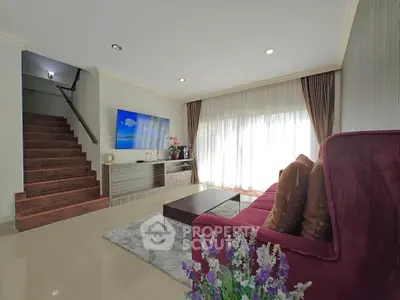 Spacious living room with modern decor and natural light, featuring a cozy sofa and elegant staircase.