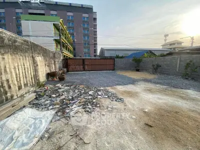 Spacious vacant lot with potential for development, featuring a secure gated entrance and urban surroundings.