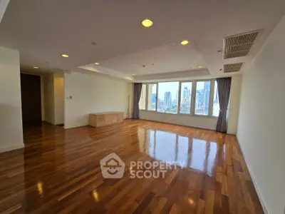 Spacious empty living room with hardwood floors and city view windows.