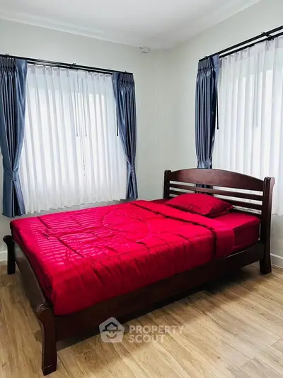 Cozy bedroom with wooden bed frame and vibrant red bedding, featuring elegant curtains and natural light.