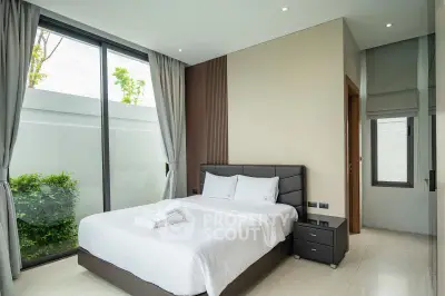 Modern bedroom with large windows and garden view, featuring elegant decor and natural light.