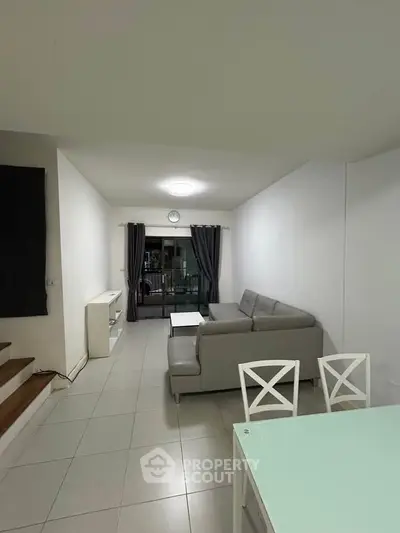 Spacious living room with modern sofa and balcony view, perfect for relaxation.