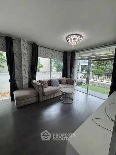 Elegant living room with plush sofa, chic chandelier, and large windows overlooking a serene garden.