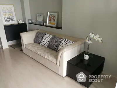 Modern living room with stylish beige sofa and decorative pillows, complemented by a sleek black side table and elegant decor.