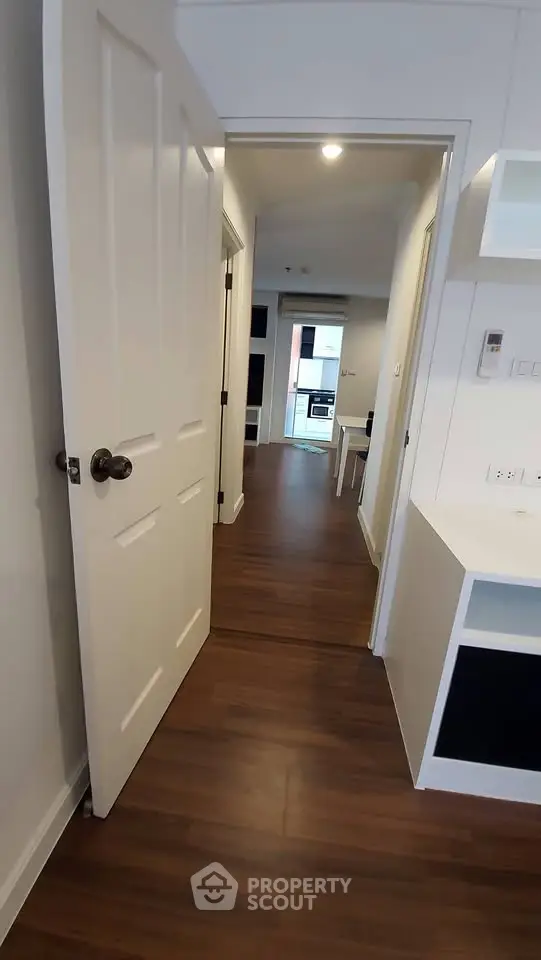 Modern apartment hallway with wooden flooring leading to a bright kitchen area.