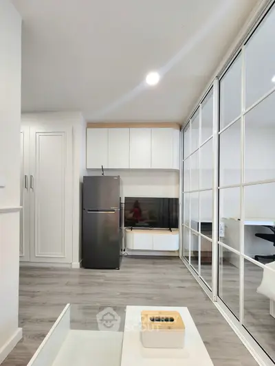 Modern living room with sleek design, featuring a glass partition, stylish furniture, and a stainless steel fridge.