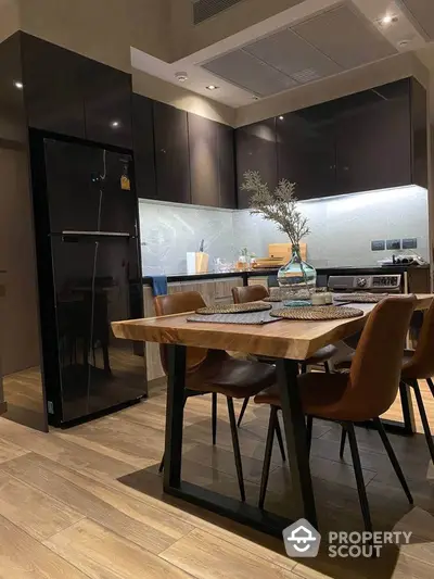 Modern kitchen with sleek black cabinets and wooden dining table, featuring stylish decor and contemporary appliances.