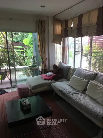 Cozy living room with large windows and garden view, featuring a comfortable sofa and modern decor.