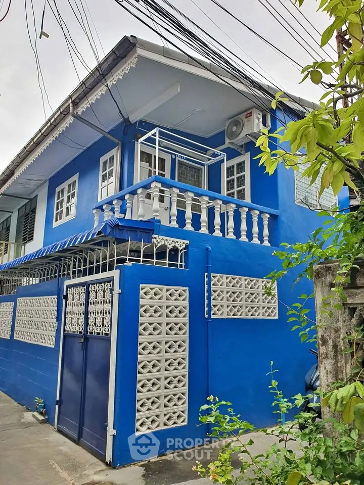 Charming blue house with decorative balcony and lush greenery, perfect for cozy living in a vibrant neighborhood.