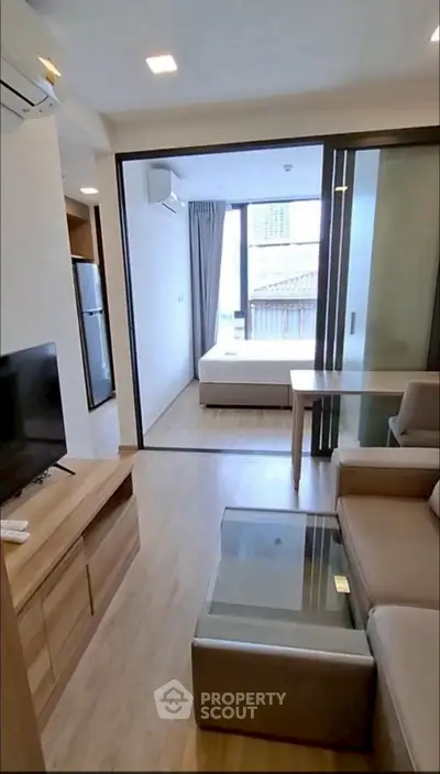 Modern apartment with open living room and bedroom, featuring sleek furniture and natural light.