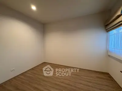 Spacious empty room with wooden flooring and natural light from window.