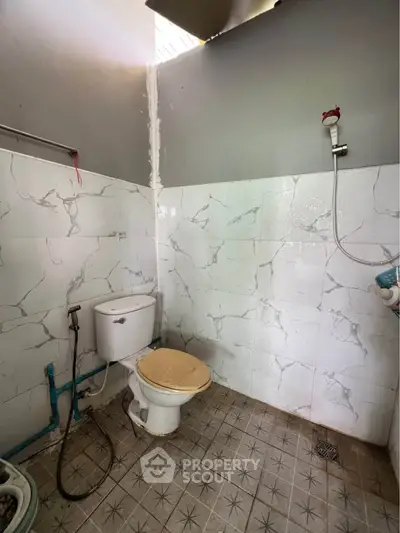 Simple bathroom with tiled walls and floor, featuring a toilet and shower setup.