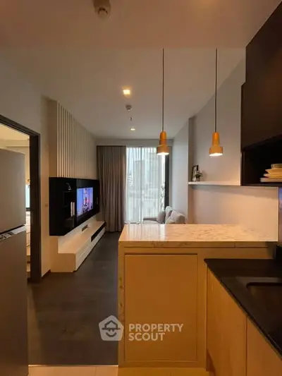 Modern open-layout living room with stylish kitchen and cozy seating area, featuring elegant lighting and contemporary design.