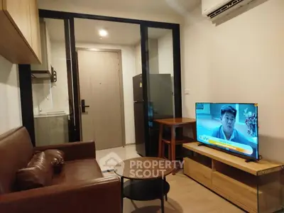 Modern living room with brown leather sofa, TV, and kitchenette in cozy apartment.