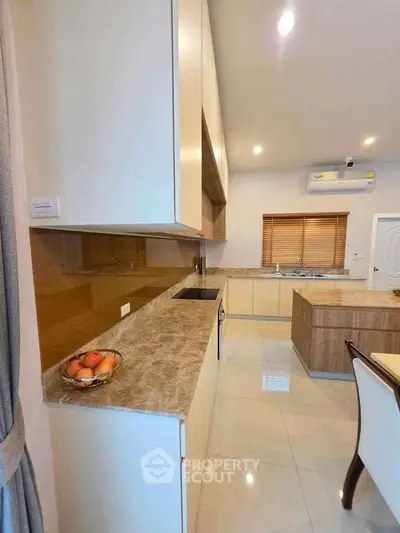 Modern kitchen with sleek cabinetry and marble countertops, featuring an open layout and dining area.