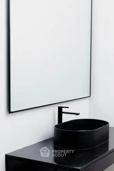Modern minimalist bathroom with sleek black sink and large mirror.