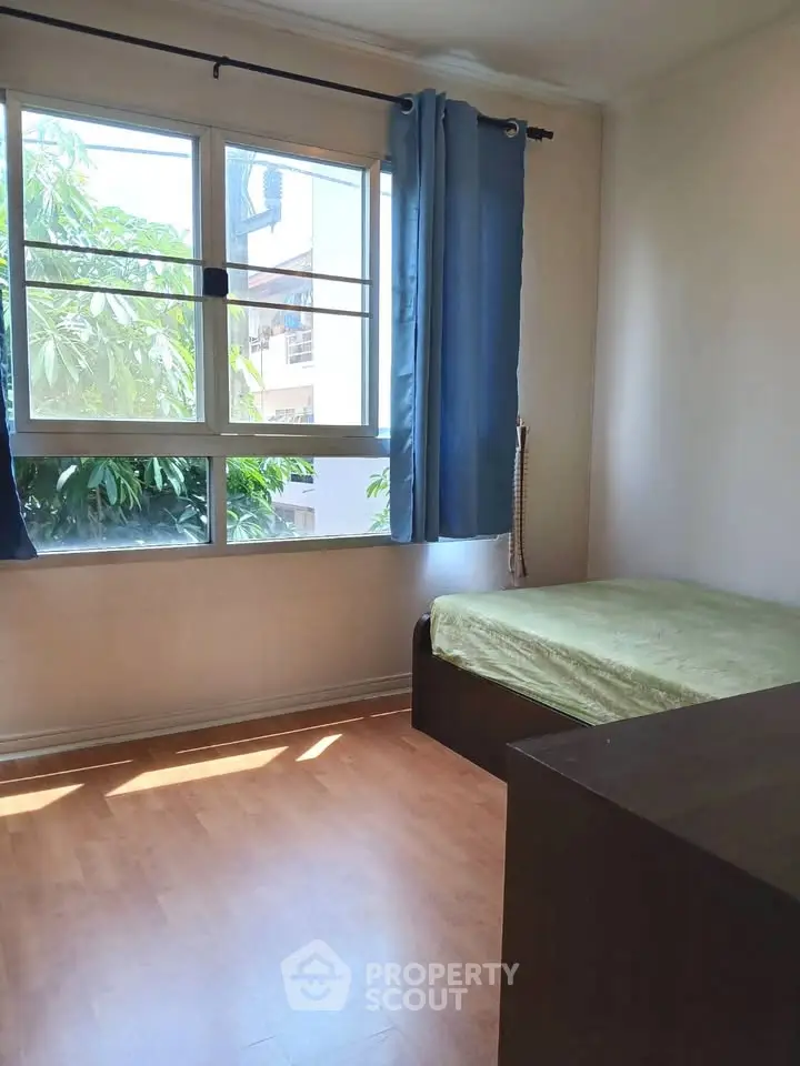 Cozy bedroom with large window and natural light, featuring a single bed and wooden flooring.