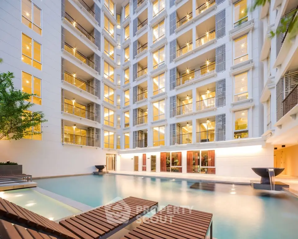 Luxurious apartment building with illuminated windows and serene poolside area.