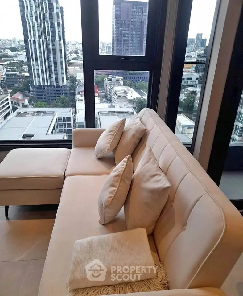 Luxurious living room with stunning city view from high-rise apartment, featuring elegant beige sofa and large windows.