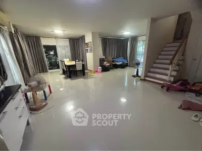 Spacious living room with modern decor and natural light, featuring a staircase and dining area.