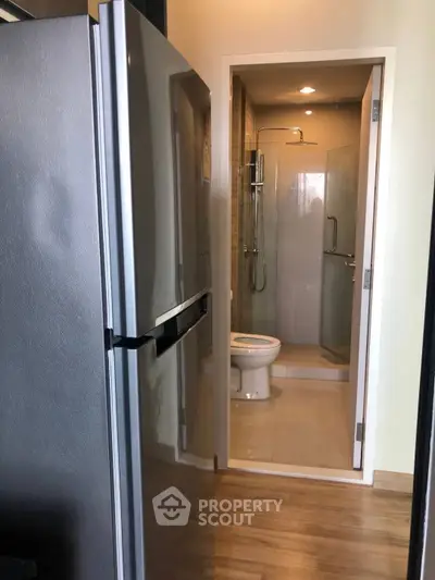 Modern bathroom with shower and adjacent refrigerator in compact space