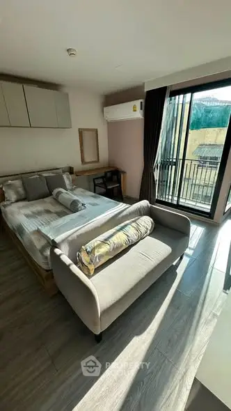 Bright bedroom with modern decor and balcony access, featuring a cozy bed and stylish sofa.