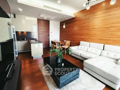 Modern living room with sleek furniture and open kitchen layout, featuring wooden accents and natural light.