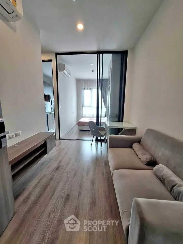 Modern apartment interior with cozy living room and glass partition leading to bedroom.