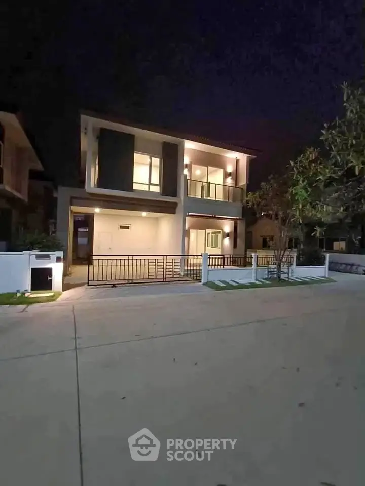 Modern two-story house with illuminated facade and spacious driveway at night.