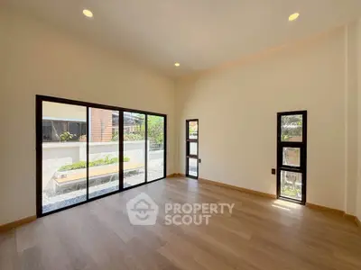 Spacious modern living room with large windows and wooden flooring, offering abundant natural light and garden view.