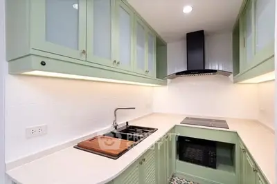 Modern kitchen with green cabinets, sleek black appliances, and stylish backsplash.
