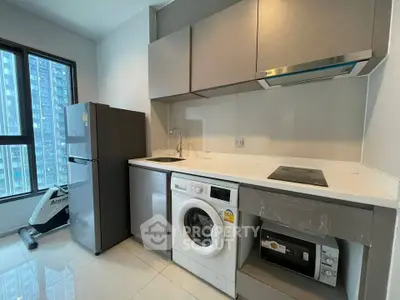 Modern kitchen with sleek cabinetry, washing machine, and large window view in urban apartment.
