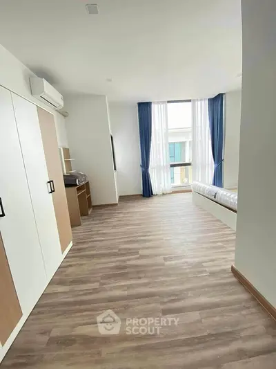 Spacious bedroom with large window and wooden flooring, perfect for natural light lovers.