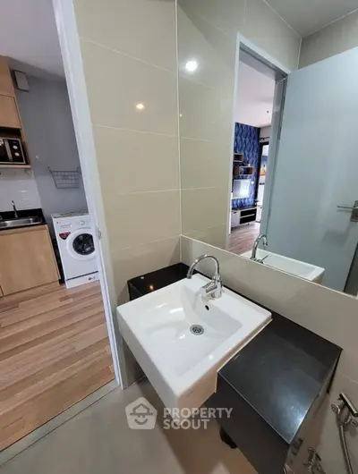 Modern bathroom with sleek sink and view into kitchen with washing machine