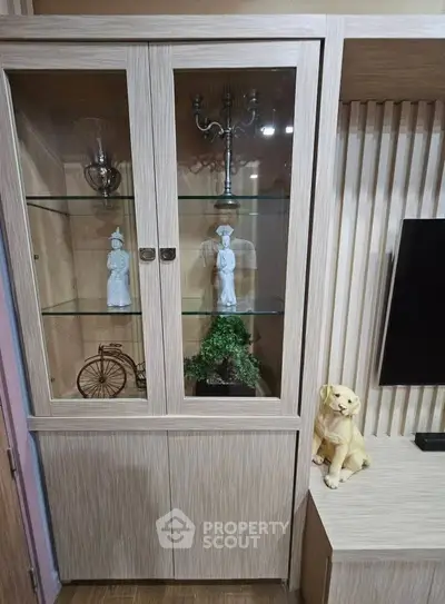Elegant wooden display cabinet with glass doors showcasing decorative items in a stylish living room setting.