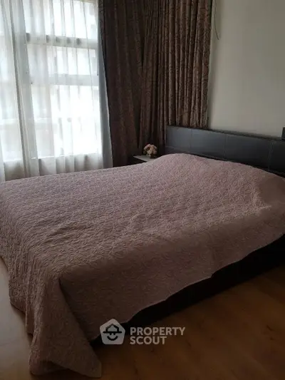 Cozy bedroom with large window and elegant curtains, featuring a neatly made bed and wooden flooring.
