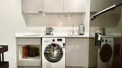 Modern kitchen with washing machine and sleek appliances in compact layout.