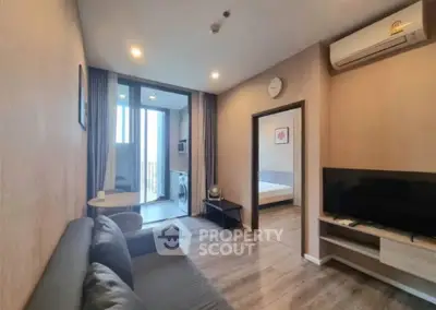 Modern living room with open layout, featuring a cozy sofa, wall-mounted TV, and access to a bedroom and balcony.