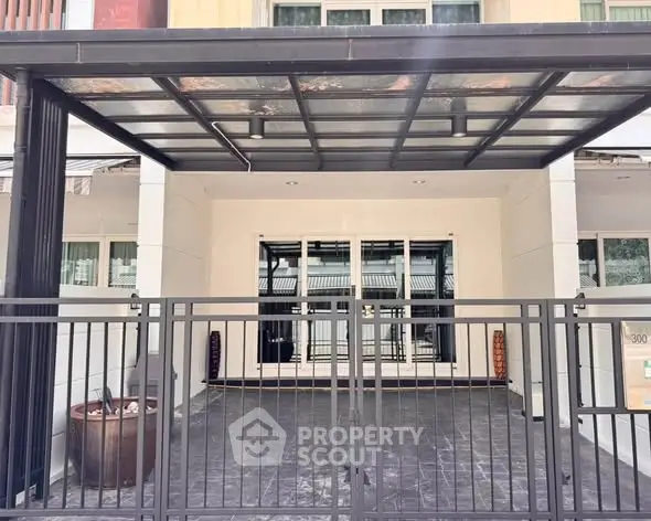 Modern house entrance with sleek metal gate and covered carport, perfect for urban living.