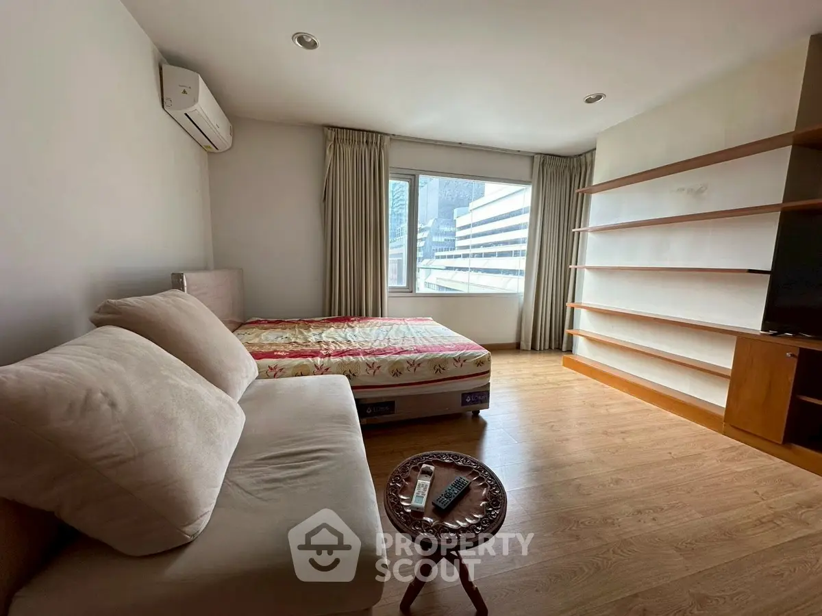 Spacious bedroom with cozy sofa and large window offering city view