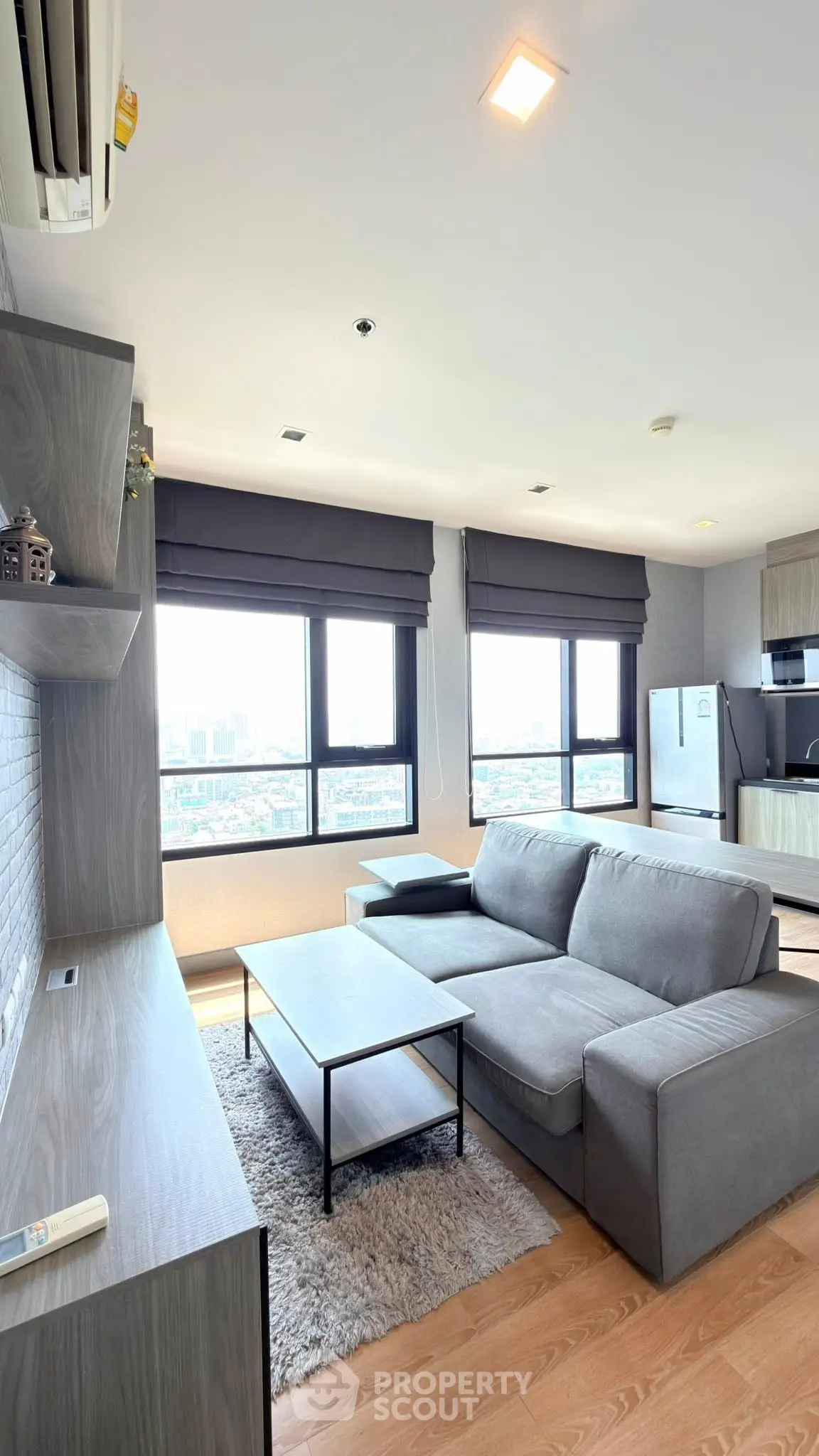 Modern living room with large windows and city view, featuring a cozy gray sofa and sleek wooden furniture.