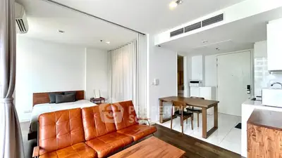 Modern open-plan living room with stylish leather sofa and adjacent bedroom in a contemporary apartment.