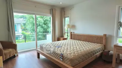 Spacious bedroom with large window and balcony view, featuring wooden furniture and natural light.